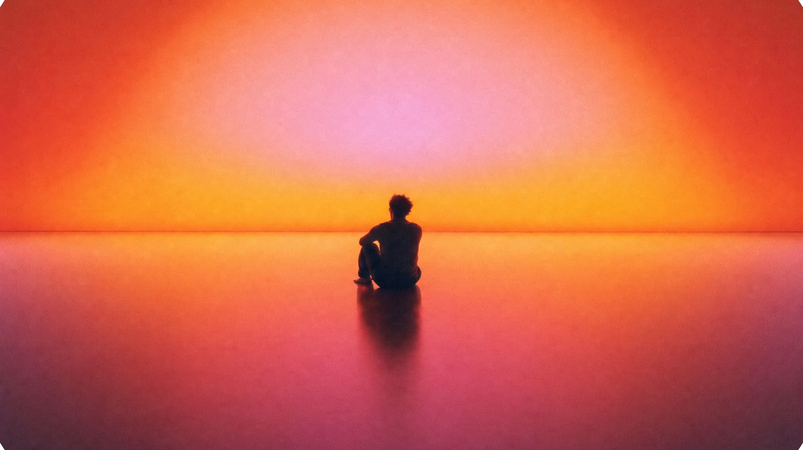 Silhouette of a person sitting on a reflective surface, looking toward a bright, colourful orange and pink horizon.